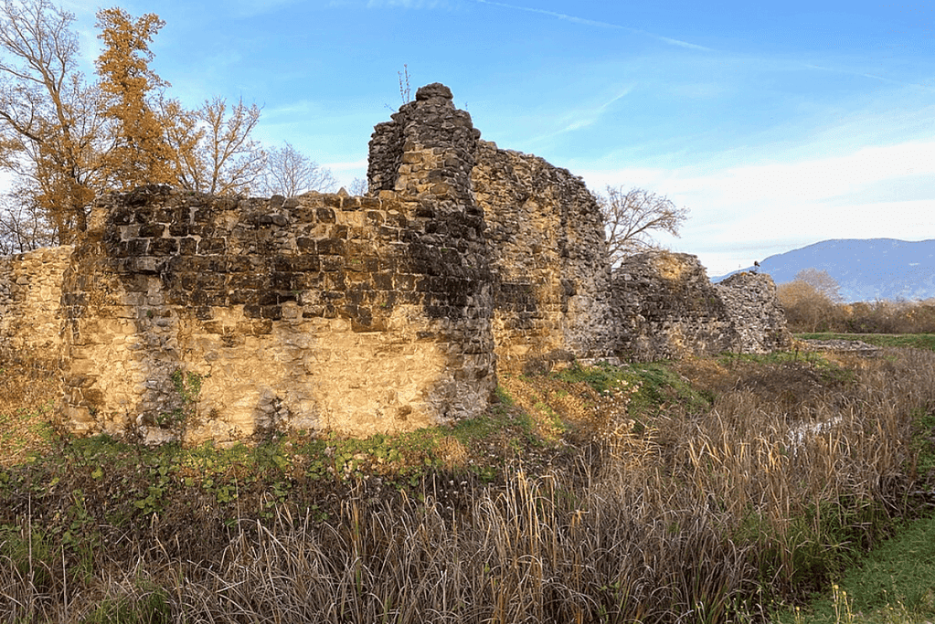 Image of the weathered stone remnants of Rouelbeau Castle amidst overgrown foliage, once the dwelling of the scary historical figure, the White Lady, set against a somber sky.