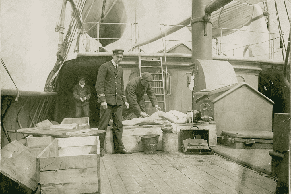 Image of a crew member overseeing the embalming process for a recovered body on the deck of a rescue ship that came to aid the Titanic survivors.
