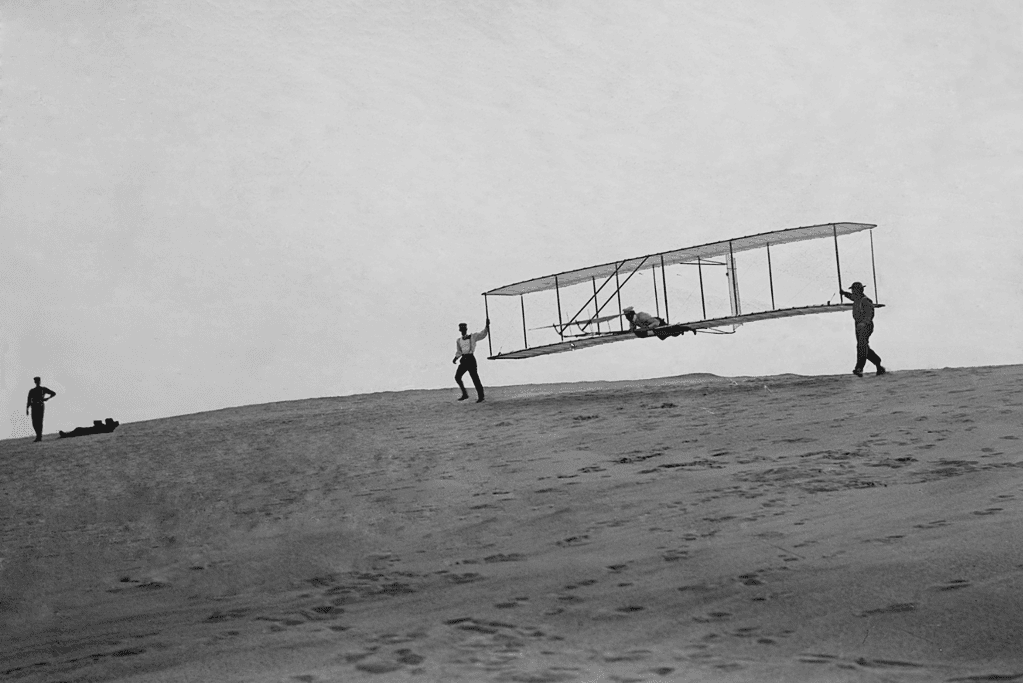 Wilbur Wright piloting the airplane while brother Orville holds on at Kitty Hawk, North Carolina